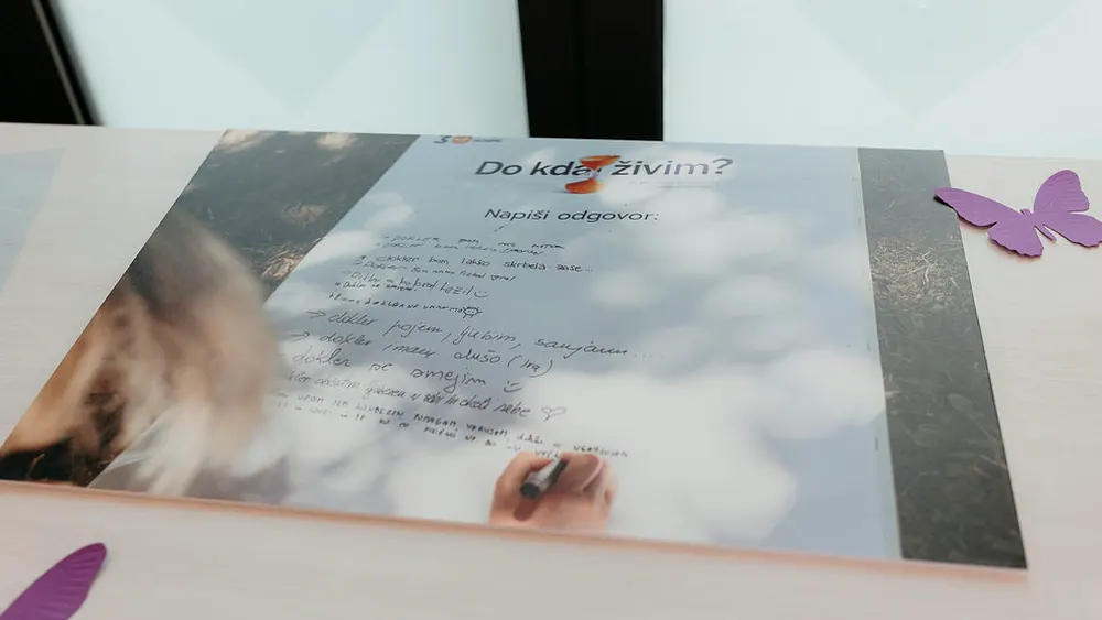 Kartica z vprašanjem »Do kdaj živim?« in rokopisnimi odgovori obiskovalcev na mizi.